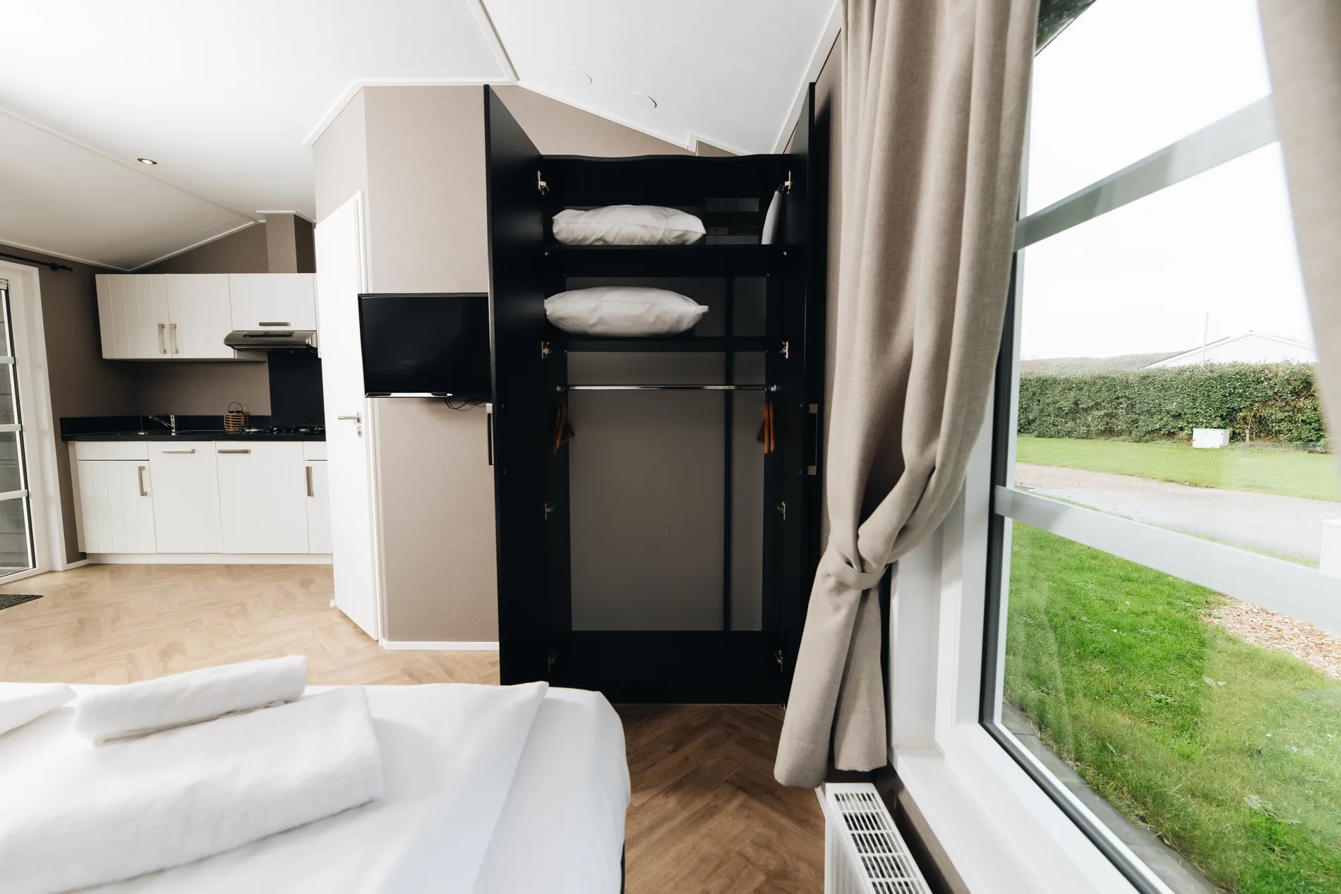 Open kledingkast met extra kussens in een ruime hotelkamer, met zicht op de tv en de keukenfaciliteiten.